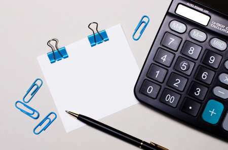On a light background, a calculator, a pen, blue paper clips and a blank sheet of paper to insert text or illustrations. Template. Top view with copy spaceの写真素材