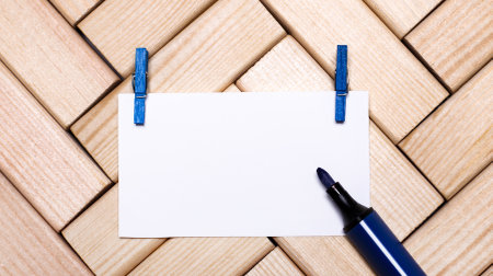 On a wooden background, a white blank card for inserting text on blue clothespins and a blue marker. Top view with copy space. Templateの写真素材