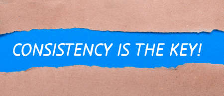 A strip of blue paper with the words CONSISTENCY IS THE KEY between the brown paper. View from aboveの写真素材