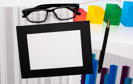 On the desktop there are reports, charts, black-framed glasses, a pen and a sheet of paper in a...