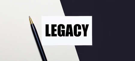 On a black and white background lies a pen and a white card with the text LEGACY.の写真素材