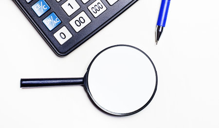Magnifier, calculator and blue ballpoint pen on a light background. View from above. Business...