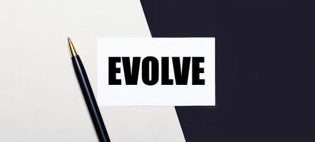 On a black and white background lies a pen and a white card with the text EVOLVE