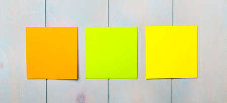On a light blue wooden background, there are three colored stickers for writing. Template. Copy spaceの写真素材
