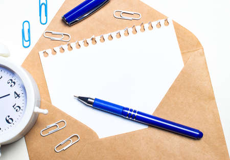 On a light background, an open envelope, a white alarm clock, white and blue paper clips, a blue pen and a sheet of paper with a place to insert text. Templateの写真素材