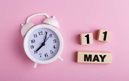 On a pink background, a white alarm clock and wooden cubes with the date of MAY 11の写真素材