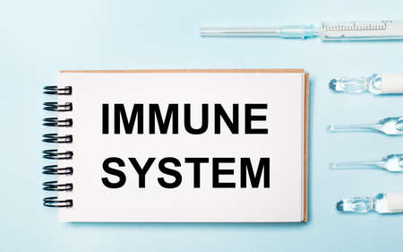 On a blue background ampoule with medicines and a notebook with the text IMMUNE SYSTEM. Medical conceptの写真素材