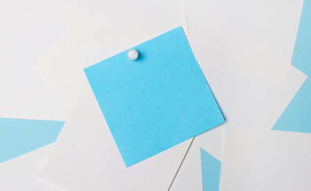 On a light blue background, white square pieces of paper. A light blue square sticker is pinned to them with a white paper clip. Template. Copy spaceの写真素材
