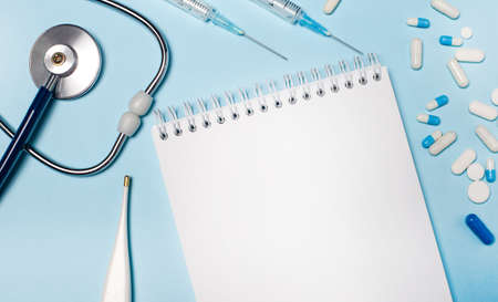 On a light gray background, a stethoscope, an electronic thermometer, pills, syringes and a notebook with a place to insert text. Medical concept. Templateの写真素材