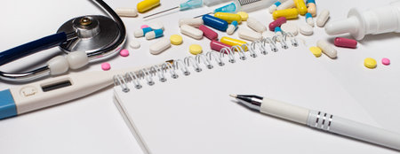 On a light background lies a stethoscope, bright multi-colored pills and a notebook with a pen....