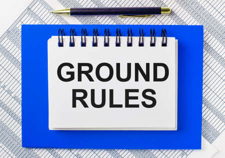 Against the background of reports on the desktop, a blue notepad. It has a pen and a white notebook with the text GROUND RULES. Business conceptの写真素材