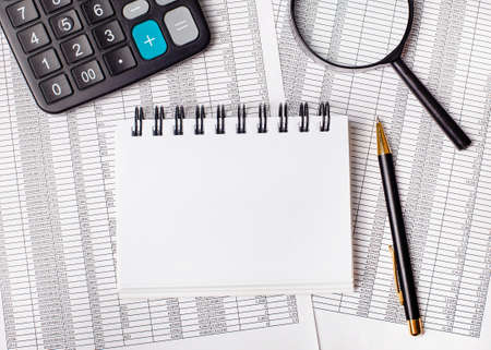 On the table are reports, a magnifying glass, a calculator, a pen and a white notebook with space to insert text or illustrations. Template. Business conceptの写真素材