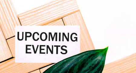 On a white background wooden building blocks, a white card with the text UPCOMING EVENTS and a green...