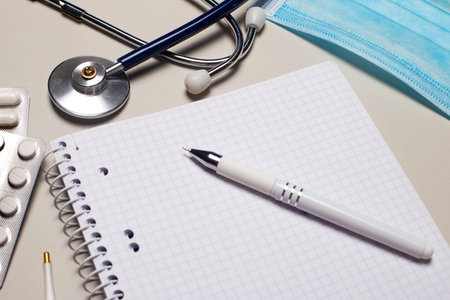 On a light gray background, a medical mask, a stethoscope, pills and a notebook with a pen. Medical conceptの写真素材