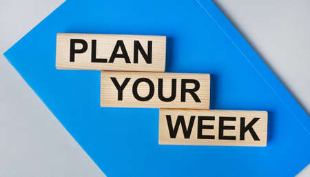 There is a blue notebook on a light gray background. Above are three wooden blocks with the words PLAN YOUR WEEK.の写真素材