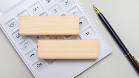Wooden blocks with a place to insert text lie on a light background on a white calculator. Nearby is...