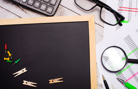 On the desktop there is a calculator, reports, glasses, a magnifying glass, pens and a board with a...
