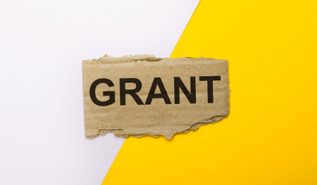 On a white and yellow background, brown torn cardboard with the text GRANT