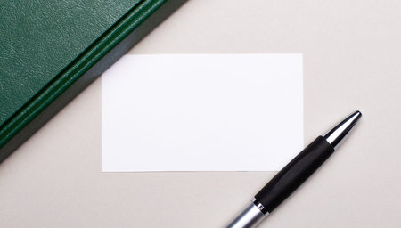 On a light gray background lies a pen, a green notebook and a white blank card with a place to insert text. Business concept. Templateの写真素材