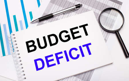 On the table are reports, diagrams, a pen, a magnifying glass and a white notepad with BUDGET DEFICIT text. Business conceptの写真素材