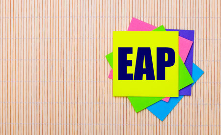 On a light wooden background, bright multicolored stickers with the text EAP Employee Assistance...
