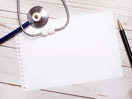 On a light wooden table there is a stethoscope, a pen and a sheet of paper with a place to insert text. Medical conceptの写真素材