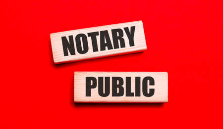 On a bright red background, there are two light wooden blocks with the text NOTARY PUBLICの写真素材