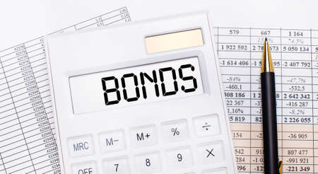 On the desktop there are reports, a white calculator with the text BONDS on the scoreboard and a pen. Business concept.の写真素材