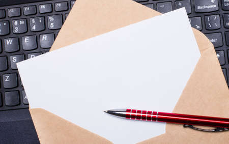 White blank card with craft envelope on work desk with modern laptop keyboard and burgundy pen. Flat layout of the workplace. Copy space.の写真素材