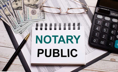On the office table there is a calculator, a pen, a notebook with the text NOTARY PUBLIC, glasses and dollars. Stylish workplace. Business conceptの写真素材