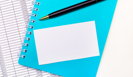 On the office desk there are reports, a light blue notepad, a black pen, and a white blank card with space to insert text. Stylish workplace. Business conceptの写真素材