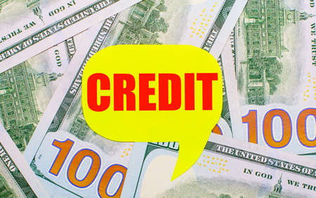 Against the background of dollars scattered on the table is a yellow curly card with the text CREDIT. Financial conceptの写真素材