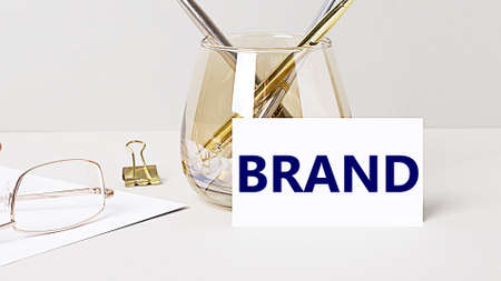 Work desk with gold glasses, pen, white card with the text BRAND. Business concept. Home Office. Workplace close-up.の写真素材