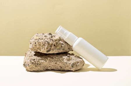 On a white and yellow background there are natural rough light stones and a white bottle with a place to insert text. The concept of medicine and beauty. Mockupの写真素材