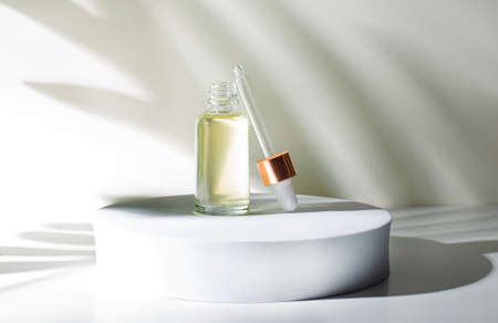 On a light green background on a round podium there is an open glass bottle with yellow oil. There is a cap with a pipette next to it. Shadows. The concept of beauty and medicineの写真素材