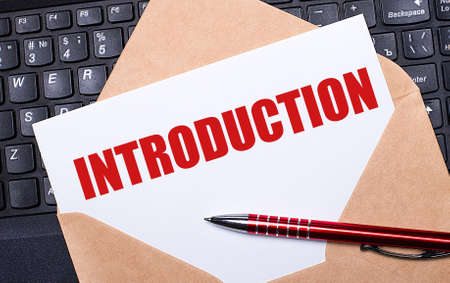 White card with the text INTRODUCTION in a craft envelope on a work desk with a modern laptop keyboard and burgundy pen. Flat layout of the workplace.の写真素材
