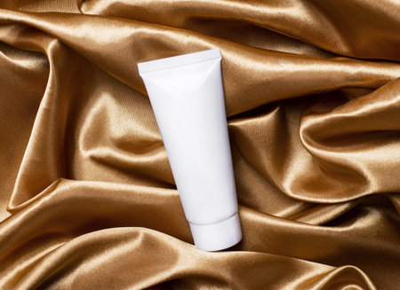 On the background of a curved golden fabric is a white cream tube with a place to insert text. The...
