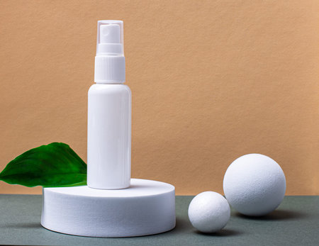 On a beige and green background, a round white podium, a green leaf of a plant and a white tube for cream or serum with a place to insert from the text. There are white balls nearby. Templateの写真素材