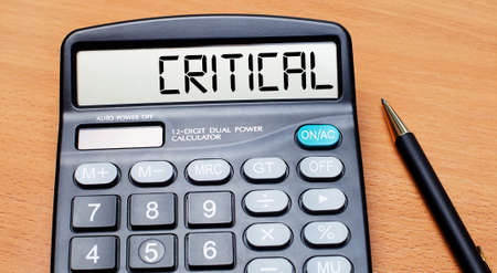On a wooden table there is a black pen and a calculator with the text CRITICAL. business conceptの写真素材