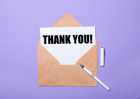 On a purple background, a white pen, a craft envelope and a white card with the text THANK YOU. view...