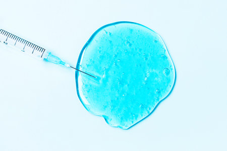 A drop of a clear blue gel-like liquid and a syringe. beauty and health cosmetics. Anti-aging...