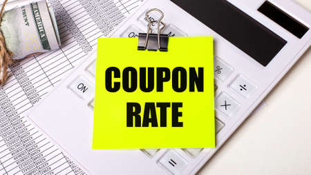 On a light background - cash, a white calculator and a yellow sticker under a black paper clip with the text COUPON RATE. business conceptの写真素材
