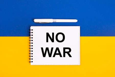 A white notebook with the text NO WAR and a white pen on a blue and yellow background.の写真素材