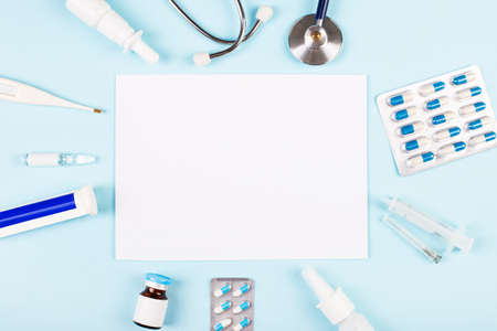 On a blue background are a stethoscope, a thermometer, pills, medicine bottles and a piece of paper with space to insert text inside. view from above. medical conceptの写真素材