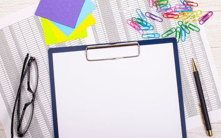 An empty notebook with a pen, reports, bright stickers, paper clips and glasses lies on a white...