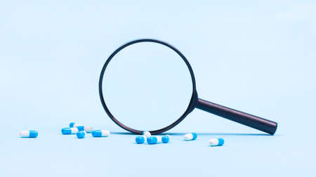 On a blue background, white-blue pill capsules and a black magnifying glass with a place to insert text. medical concept. copy spaceの写真素材