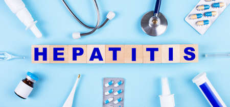 On a blue background, a stethoscope, a thermometer, other medicines and wooden cubes with the text HEPATITIS. view from above. medical conceptの写真素材