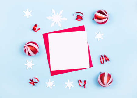 christmas composition. Blank paper, Christmas red balls, white snowflakes on a light blue background. Flat lay, top view, copy space. Holiday card with place to insert textの写真素材