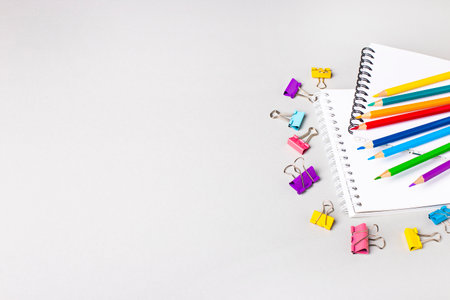 Notebooks, colored pencils and paper clips on a light gray table. Place to copy. Bannerの写真素材