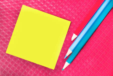 Blank yellow sticker for notes on a burgundy background with colorful pencils. Sticky note paper mockup. note ideas. Business discussion, teamwork, brainstorming conceptの写真素材